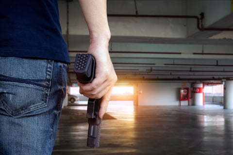 Back view of man holding a gun in car park, copy space for text.