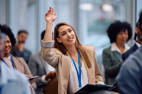 Young happy businesswoman raising hand to ask a question while attending a seminar in conference hall.
