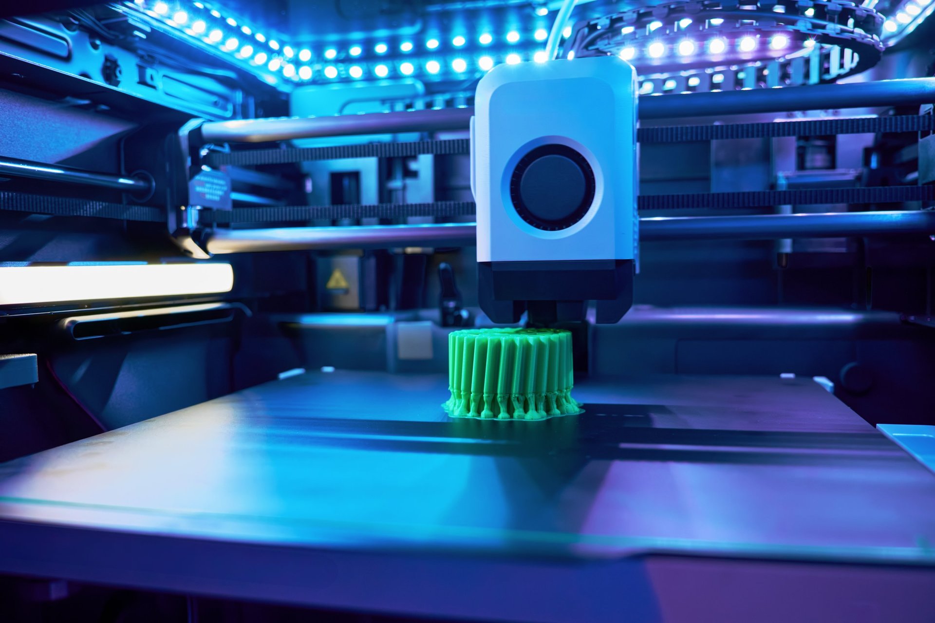 A 3D printer is in action, meticulously producing a vibrant green cylinder with intricate details under bright LED lighting
