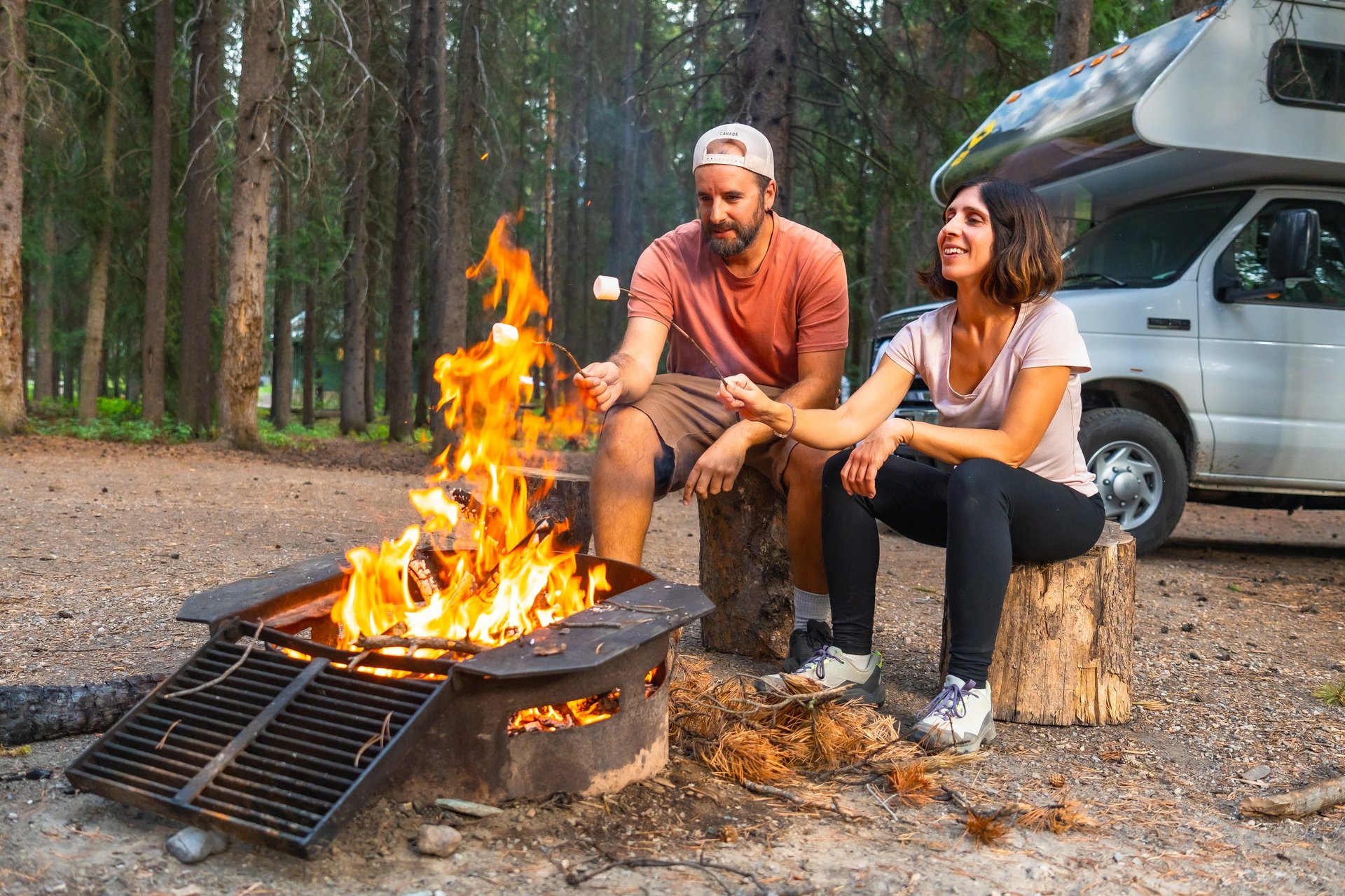 Tourists roasting marshmallows over a campfire near their camper van in banff national park, canadian rockies, alberta, enjoying a relaxing evening in nature