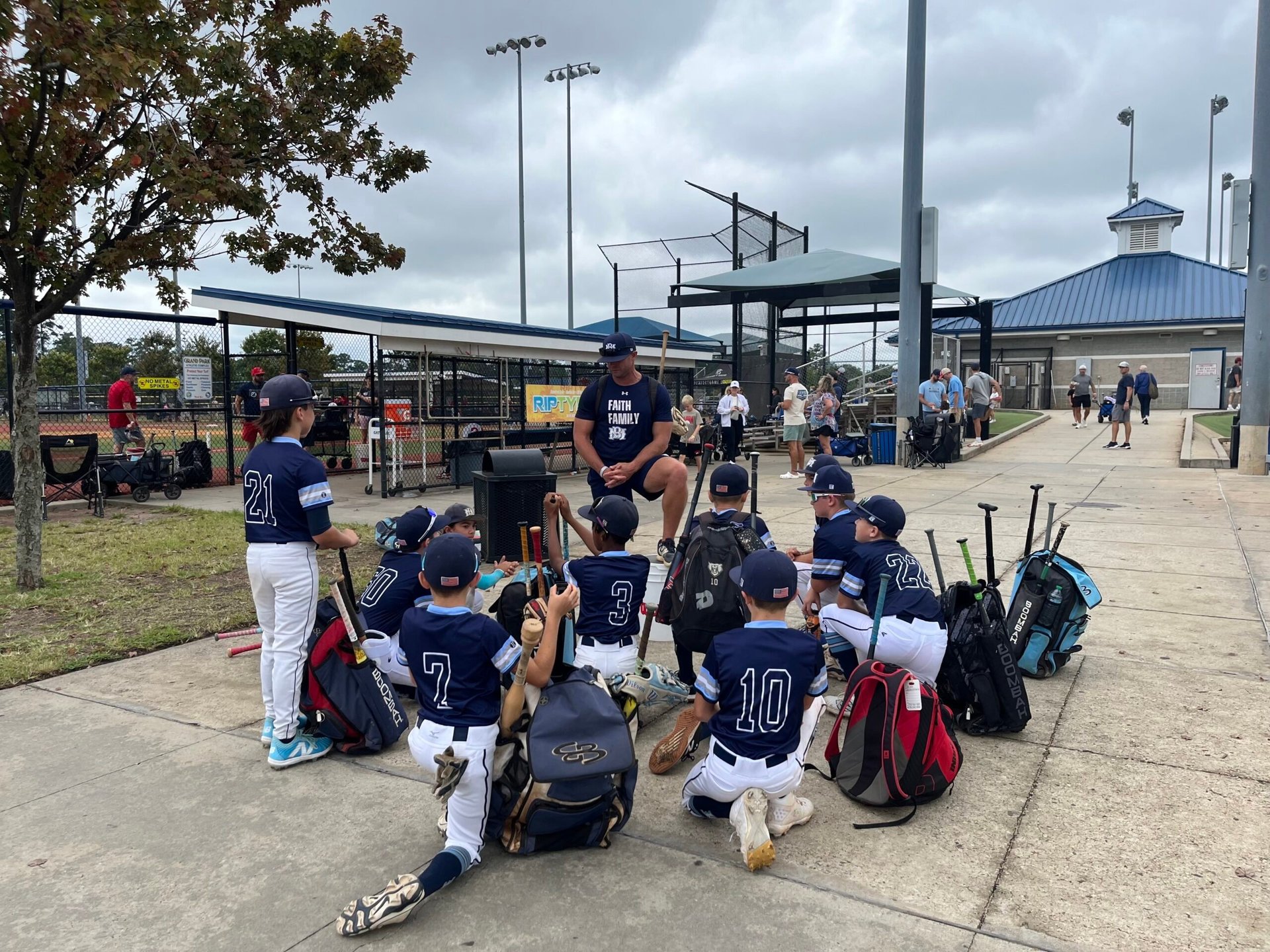Youth baseball team huddled together on field at outdoor sports complex with field lights and dugout visible