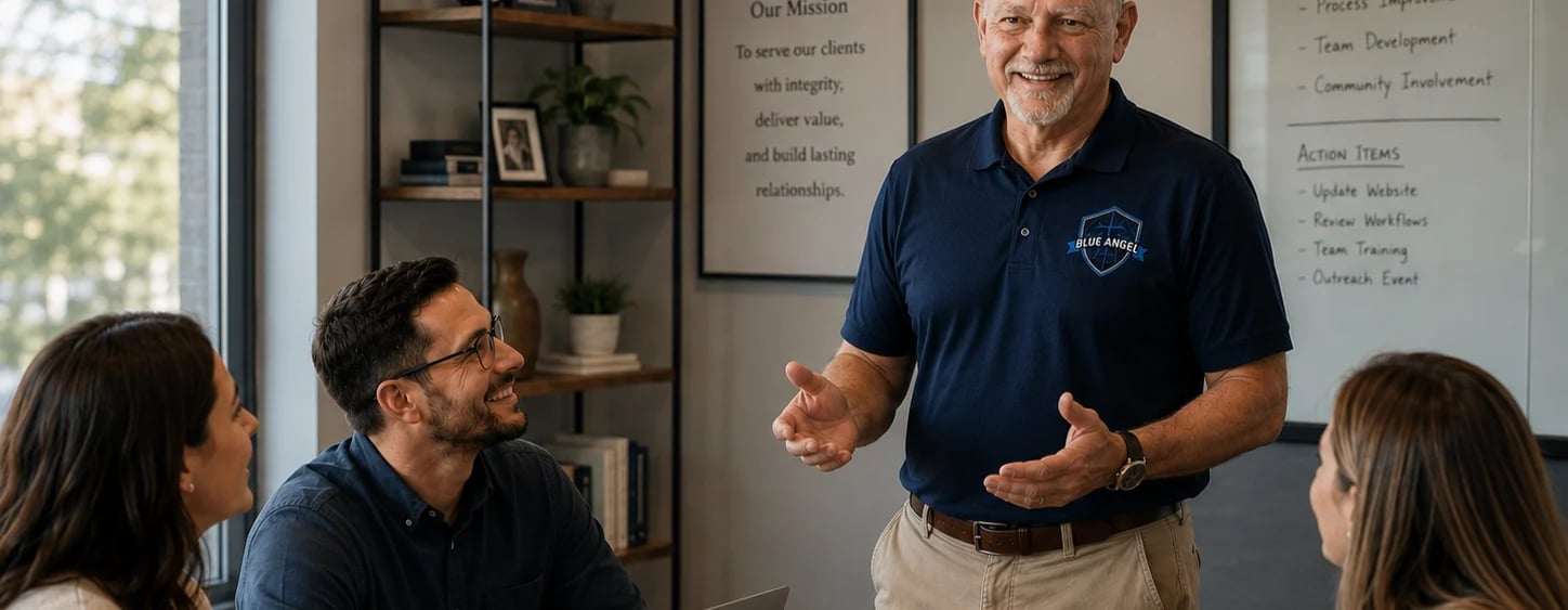 Older man in blue polo shirt speaking to three seated colleagues in an office meeting room