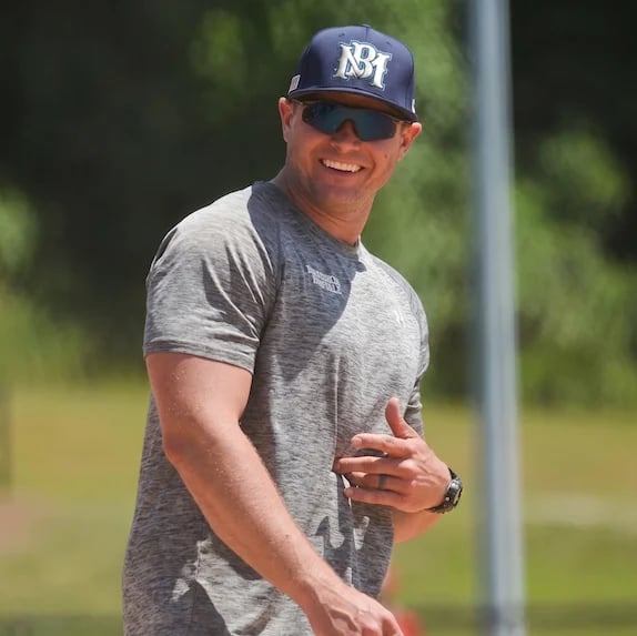 Man in gray t-shirt and navy baseball cap with sunglasses smiling outdoors